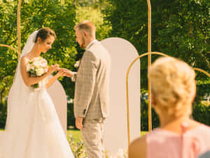 新娘和新郎在花園的金色拱門下交換結婚戒指。 — 婚禮 壁紙