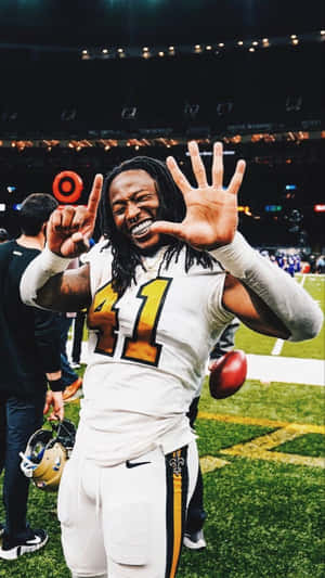 號碼41的足球運動員在夜間燈光璀璨的球場上高舉雙臂慶祝。 — Alvin Kamara 壁紙