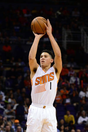 籃球運動員在擁擠的場館中投出跳投。 — Devin Booker 壁紙