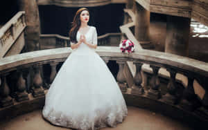 一位身穿白色婚紗的新娘，在石陽台上手持粉白色花束。 — 婚紗 壁紙