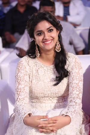 一位身穿白色蕾絲裙的微笑女性坐在活動中。 — 沙希德·卡普爾 壁紙