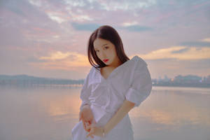 夕陽下穿白色襯衫的女子在水邊，遠處有城市燈光 — 청하 壁紙
