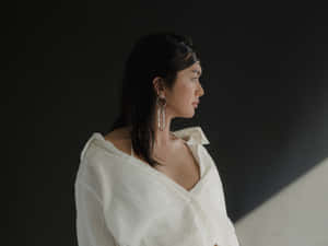 身穿白色襯衫、戴著大耳環的女性在昏暗的攝影棚燈光下若有所思地看向一旁。 — 桌面 壁紙