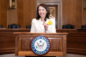 身穿白色西裝的女性在參議院講台上微笑，帶有官方印章。 — 政治 壁紙