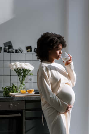 孕婦在明亮的廚房裡喝牛奶，旁邊有白花。 — 懷孕 壁紙