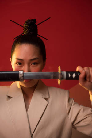 身穿米色西裝的女性在紅色背景前以強烈目光握著武士刀 — 日本武士 壁紙
