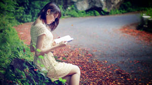 女性在秋天落葉覆蓋的小徑上閱讀一本書。 — 閱讀 壁紙