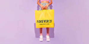 在薰衣草背景前拿著一個黃色Forever 21購物袋的人。 — 永遠21 壁紙