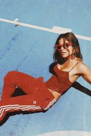 身穿紅色Adidas運動服和太陽眼鏡的女性在藍色表面上休息。