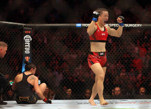 女性MMA拳手在擊敗對手後於八角籠中慶祝勝利。 — 運動 壁紙