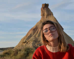 身穿紅色毛衣和眼鏡的女性在沙漠岩層附近欣賞日落。 — 晚安 壁紙