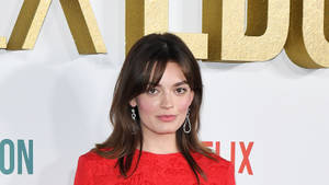 在Netflix活動中穿紅色連衣裙的女性，身後有金色字母。 — 艾瑪·華森 壁紙