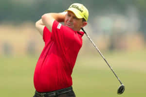 身穿紅色襯衫和黃色帽子的高爾夫球手在高爾夫球場上揮桿中。 — 運動 壁紙