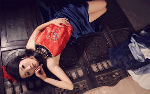 一位身穿紅藍傳統服飾的女性躺在木地板上。 — 模特兒 壁紙