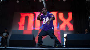饒舌歌手在紅燈下穿著紫色球衣和太陽眼鏡在舞台上表演。 — DMX 壁紙
