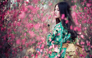 身穿綠色花卉和服的女士在春日花園中被粉紅色花朵環繞。 — 粉色花朵 壁紙