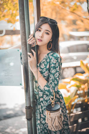 身穿花卉連衣裙的年輕女性靠著柱子，身後有秋葉。 — 模特兒 壁紙