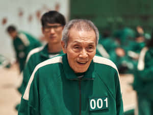 一位身穿綠色號碼運動服的長者在遊戲場景中燦爛地微笑。 — 067 魷魚遊戲 壁紙