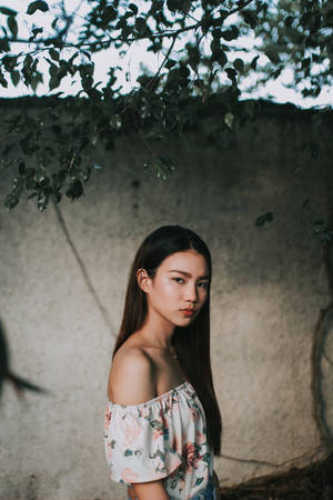年輕女性穿花卉上衣站在混凝土牆附近的樹枝下 — 曼谷 壁紙