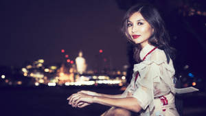 身穿白色連衣裙的女性在夜晚坐在水邊，身後有城市燈光。 — 美學天空 壁紙