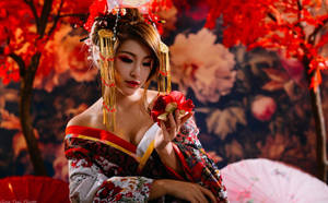 一位身穿傳統和服的藝妓，在秋樹下持著一朵紅花。 — 酷 壁紙