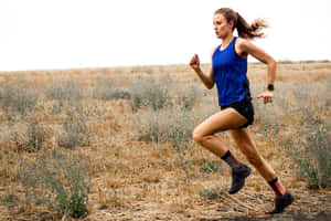 一位身穿藍色背心的女性在乾燥的草地上奔跑。 — Running 壁紙