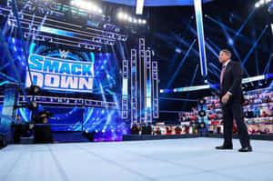 身穿西裝的WWE SmackDown主持人站在摔角擂台邊緣，舞台燈光下。 — 摔角 壁紙