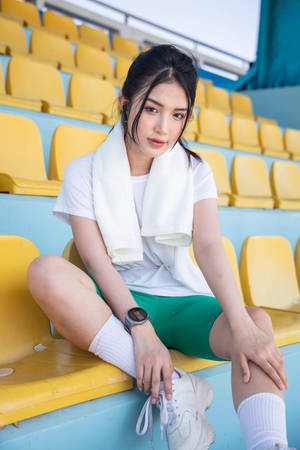 身穿運動服的年輕女性坐在體育場座位上，脖子上圍著毛巾。