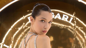 一位身穿鑲鑽連衣裙的女性在發光的Bvlgari標誌前擺姿勢。 — 瑟夏·羅南 壁紙