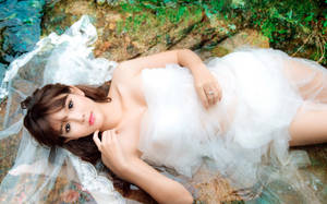 身穿白色婚紗和頭紗的女性，在清澈的水中靠著長滿苔蘚的岩石。 — 婚紗 壁紙