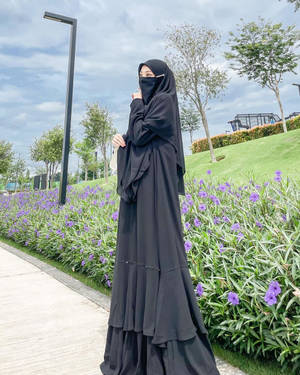 身穿黑色長袍和頭巾的女性站在公園的紫色花朵旁。 — 美麗的公主 壁紙