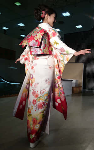 一位身穿色彩繽紛花卉圖案和服的女性，在室內伸展雙臂擺姿勢。 — 日式粉紅 壁紙