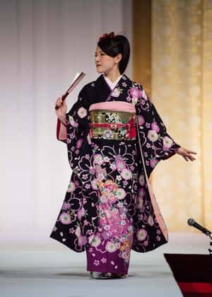 一位身穿花卉和服的女士在舞台上用扇子表演。 — 日式粉紅 壁紙