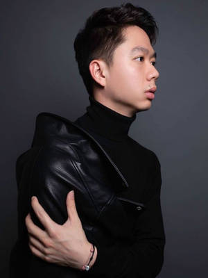 身穿黑色皮夾克和高領毛衣的年輕男子在攝影棚中手放在肩膀上站立。 — 運動 壁紙