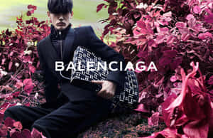 身穿黑色西裝的男子手持 Balenciaga 手袋，被洋紅色樹葉包圍。 — 巴黎世家 壁紙