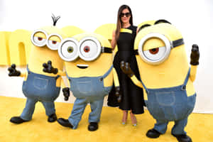 身穿黑色連衣裙的女性在活動中與三個Minion角色合影。 — 小小兵 壁紙