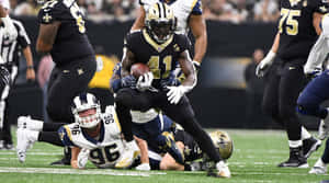 身穿黑金色球衣的美式足球員帶球奔跑並被擒抱。 — Alvin Kamara 壁紙