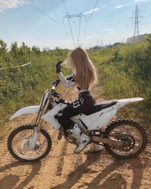 金髮女子穿著越野摩托車裝備，在草地上騎白色越野摩托車。
