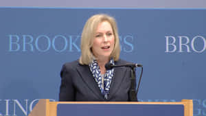 女性在講台上發言，身後有 'Brookings' 標誌。 — 華盛頓 壁紙