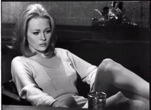 在1960年代的電影場景中，一位女性坐在桌子旁，拿著一個玻璃杯。 — 女演員 壁紙