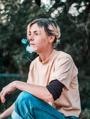 年輕女性坐在戶外綠意中呼出蒸氣。 — 抽菸 壁紙
