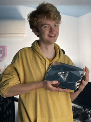 穿著黃色連帽衫的年輕男子在室內手持幾何獎盃。 — 湯米英尼特 壁紙