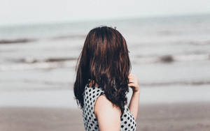 身穿波點裙的女子站在沙灘上面向海洋 — 海灘度假 壁紙