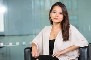 一位身穿米色開襟毛衣的女士平靜地坐在現代辦公椅上。 — 女超人 壁紙