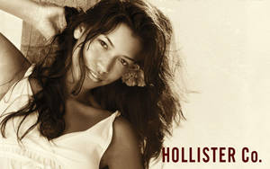 黑髮年輕女性在復古色調肖像中微笑，帶有Hollister Co.文字。 — Hollister 壁紙