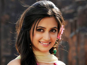 一位頭髮深色、頭上戴著粉紅色花朵、戴著綠色耳環的微笑女性。 — 克洛伊·卡戴珊 壁紙