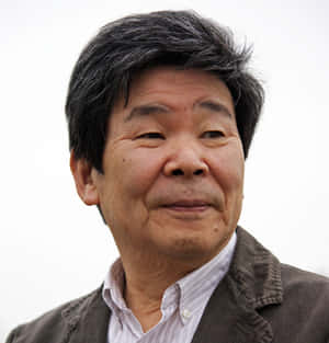 一位灰白頭髮的年長亞洲男子穿著棕色外套和條紋襯衫，露出溫柔的微笑。 — 場 圭介 壁紙
