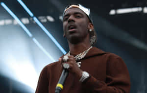 饒舌歌手在藍色燈光下拿著麥克風和金色鏈條在舞台上表演。 — Young Dolph 壁紙