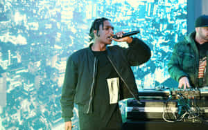 饒舌歌手在舞台上對著麥克風唱歌，背後有DJ和藍色數位螢幕。 — ASAP Rocky 壁紙