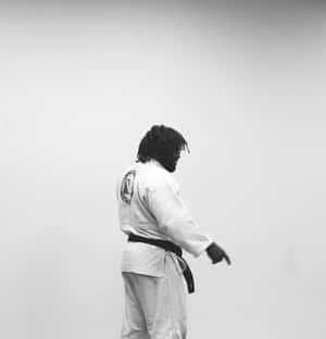 黑人武術家穿著白色道服和黑色腰帶側面站立。 — 運動 壁紙